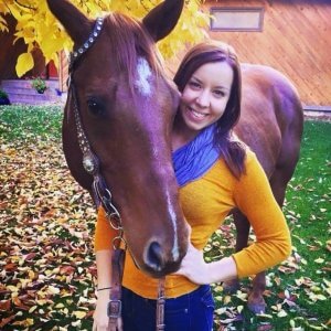 woman in yellow sweater and blue scarf with a brown horse outside in fall
