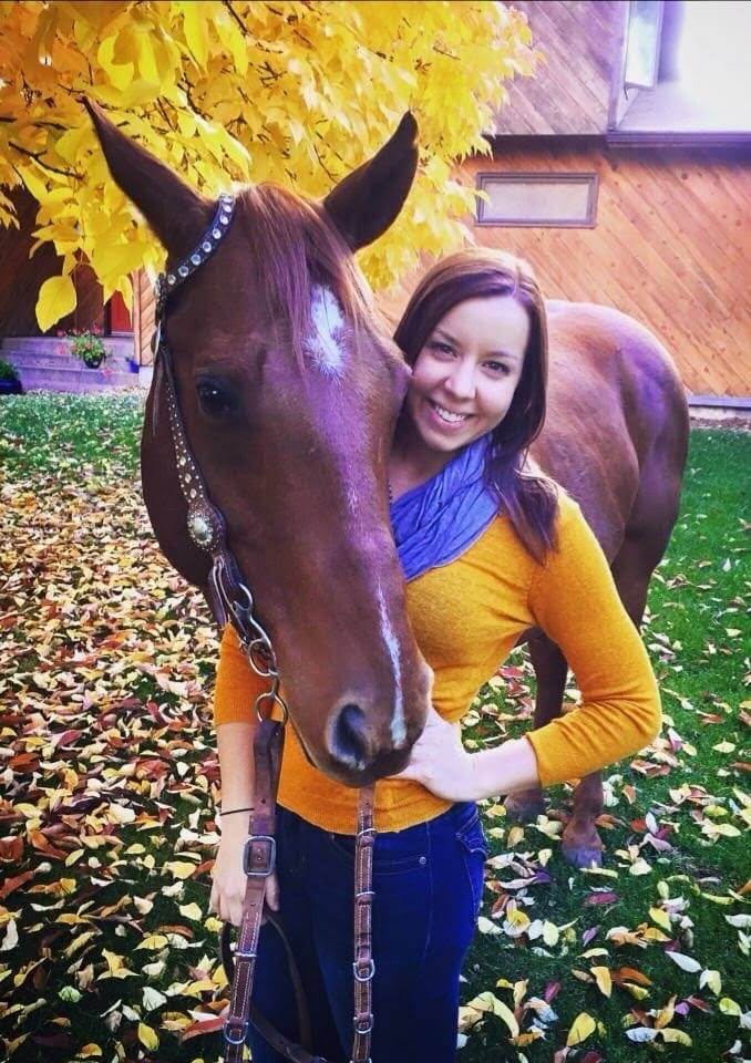 woman in yellow sweater and blue scarf with a brown horse outside in fall